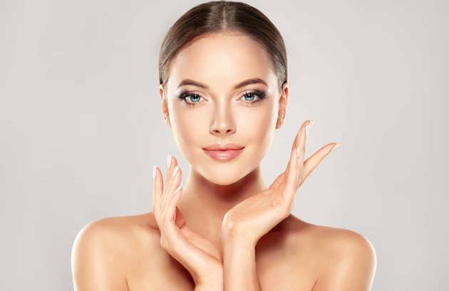 A smiling woman with clear, glowing skin frame-touching her face after a treatment by a dermatologist in Sharjah.