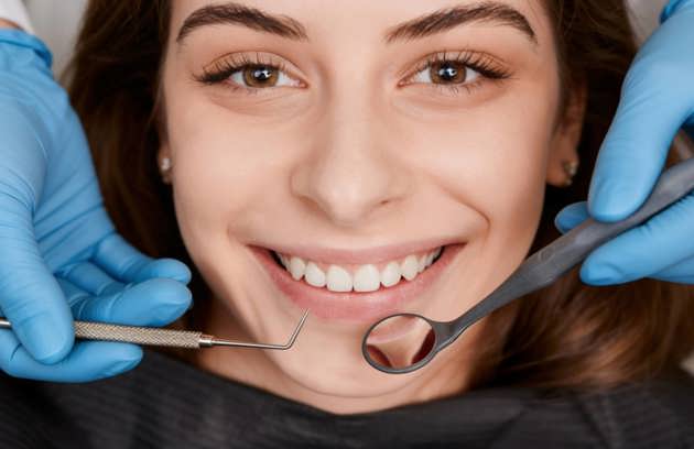 Smiling woman lying back in a dental chair during an examination by a dentist in blue gloves at a dental hospital in Sharjah